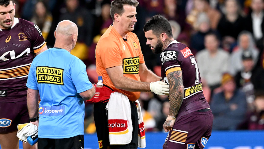 Brisbane Broncos player Adam Reynolds is treated by a trainer on the field during an NRL game.