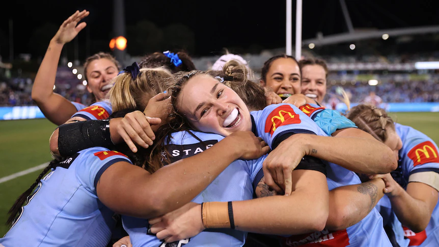 Isabelle Kelly smiles and hugs in a bundle of Blues players
