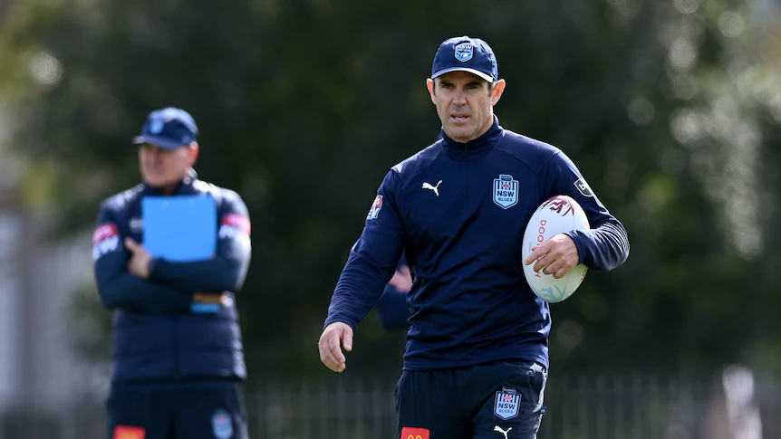 NSW State of Origin coach, Brad Fittler, holds a ball under his arm as he watches team training.