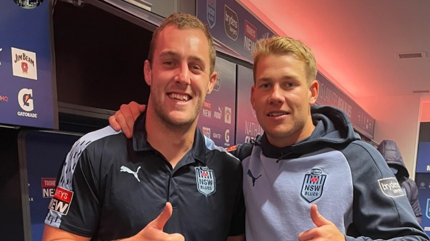 Matt Burton and Isaah Yeo standing next to each other in a team jersey and hoodie give a thumbs up.