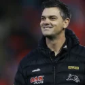 An assistant coach wearing club gear with the Penrith Panthers logo smiles as he looks across a field before a game.