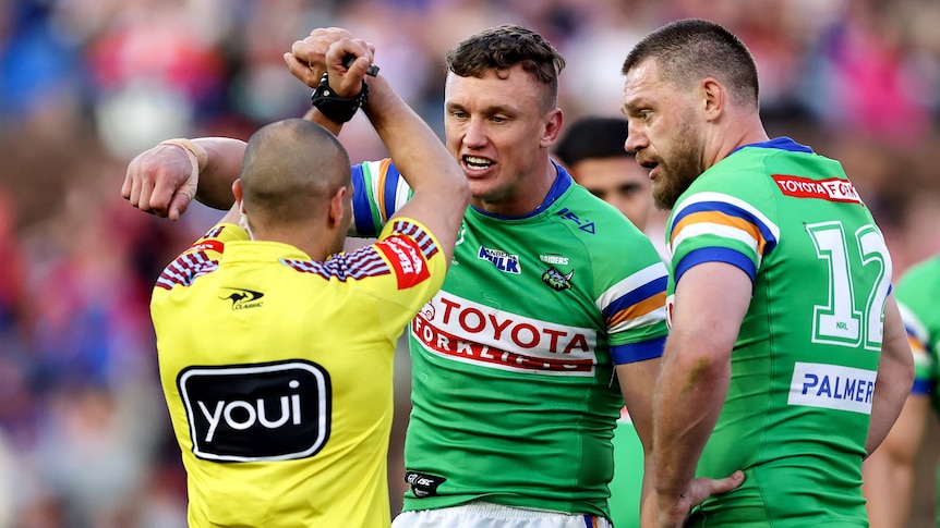 A Canberra NRL player looks at a referee who is holding his hands crossed in an 'X' shape.