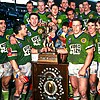 A team of men in matching green rugby jerseys stands in a group in front of a large winners plaque.