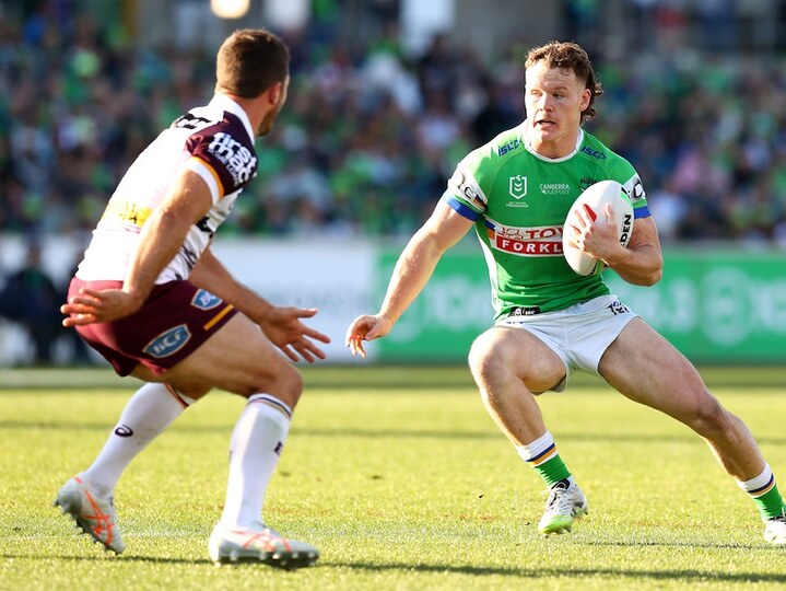 A Canberra Raiders NRL player carrying the ball steps to try and change direction and evade a Broncos defender.